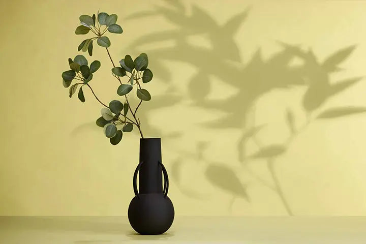 Kunstblume und Kunstzweig in Vase mit großen Schatten der Kunstblume
